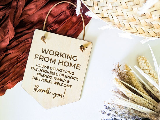 Working From Home sign with engraved text advising not to ring the doorbell or knock, with a warm tone for friends, family, and deliveries, displayed on a red fabric backdrop with dried floral accents, perfect for a home office entryway.