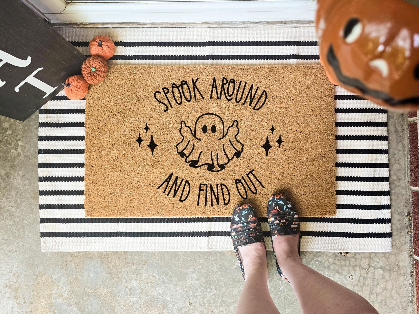 Spook Around and Find Out doormat featuring a cute ghost design with stars, displayed on a striped layering rug with decorative pumpkins, perfect for Halloween porch decor.