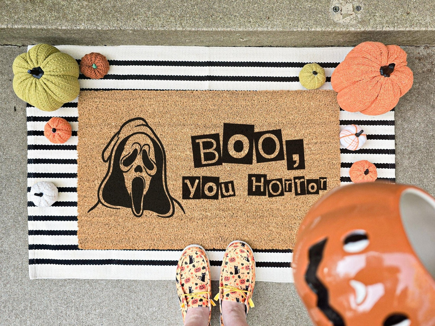 Boo, You Horror doormat featuring a ghost face design, displayed on a striped layering rug with decorative pumpkins, perfect for Halloween porch decor.